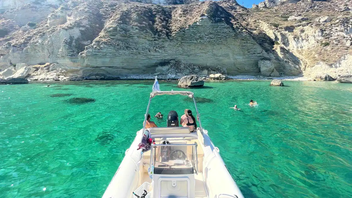 Rigid inflatable tour boat with swimmers in turquoise water under the Sella del Diavolo cliffs on a Cagliari boat tour in the Gulf of Cagliari, Sardinia