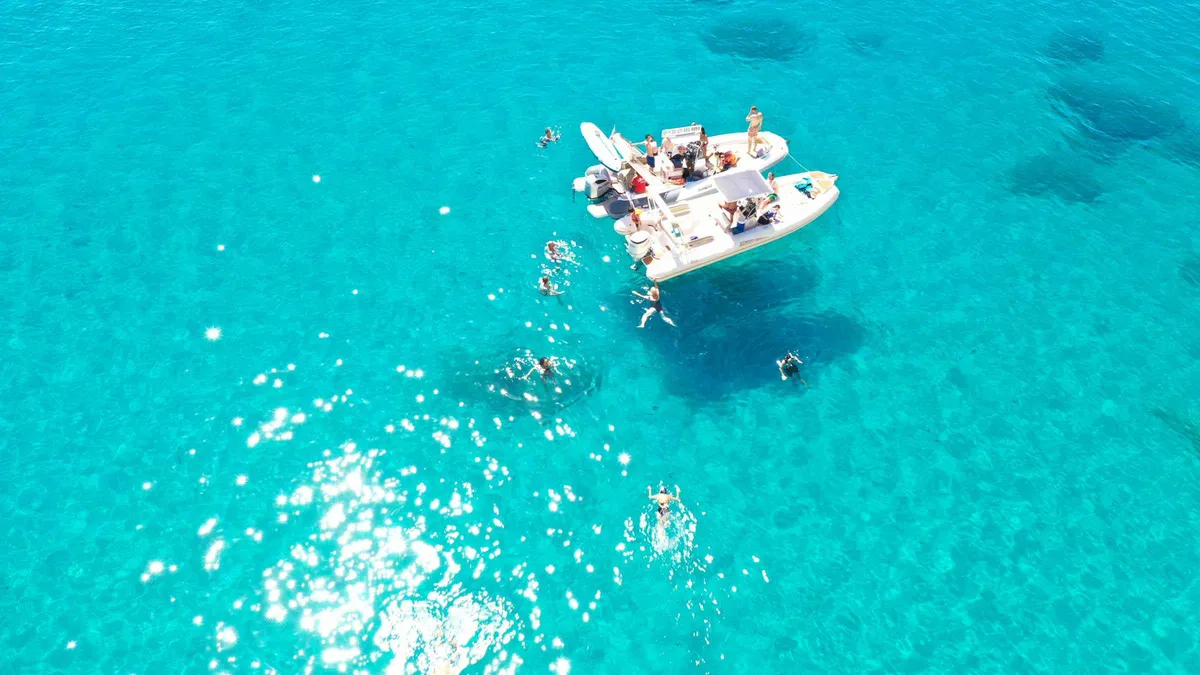 White rigid inflatable safari boat at a Sardinian cove with swimmers on a Cagliari boat tour along the Devil's Saddle coast