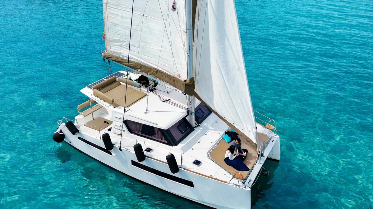 Sailing catamaran anchored below limestone cliffs with guests swimming on a Cagliari catamaran tour, Sardinia