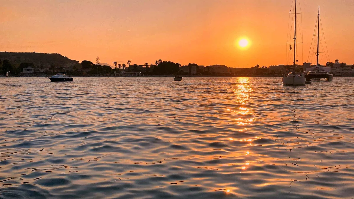 Small tour boat at anchor with guests watching the sunset over the Gulf of Cagliari on an evening boat tour in Sardinia